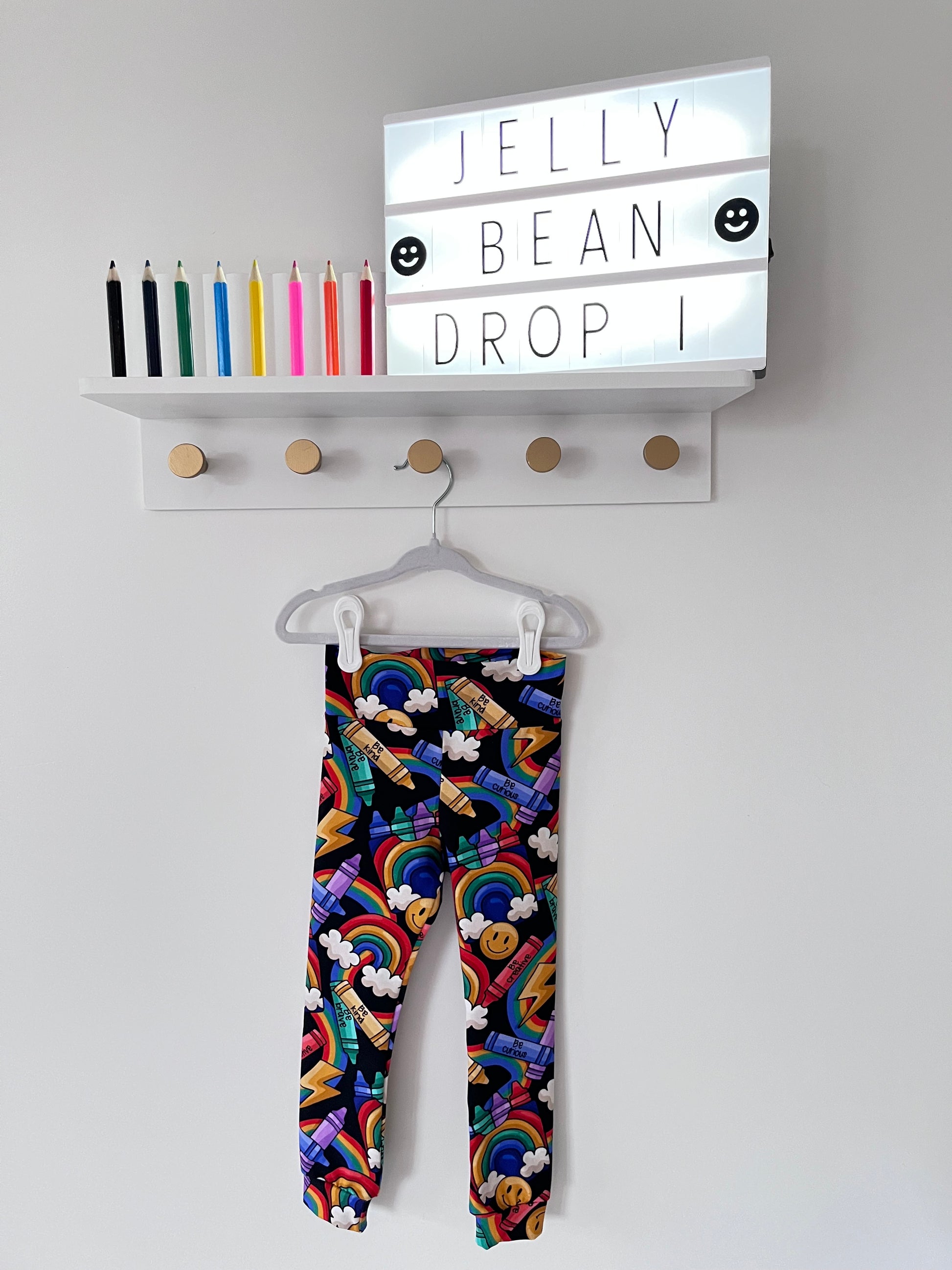 Handmade children’s leggings in a rainbow crayon print, featuring colourful crayons, rainbows, clouds, and positive messages on a dark background.