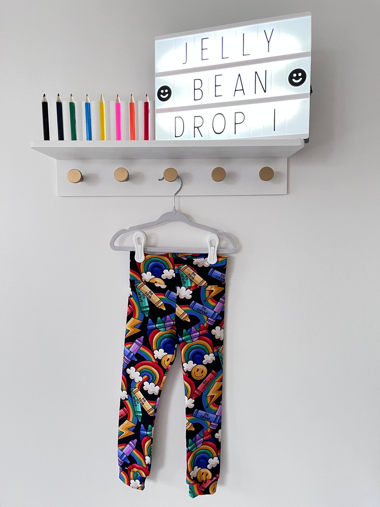 Handmade children’s leggings in a rainbow crayon print, featuring colourful crayons, rainbows, clouds, and positive messages on a dark background.
