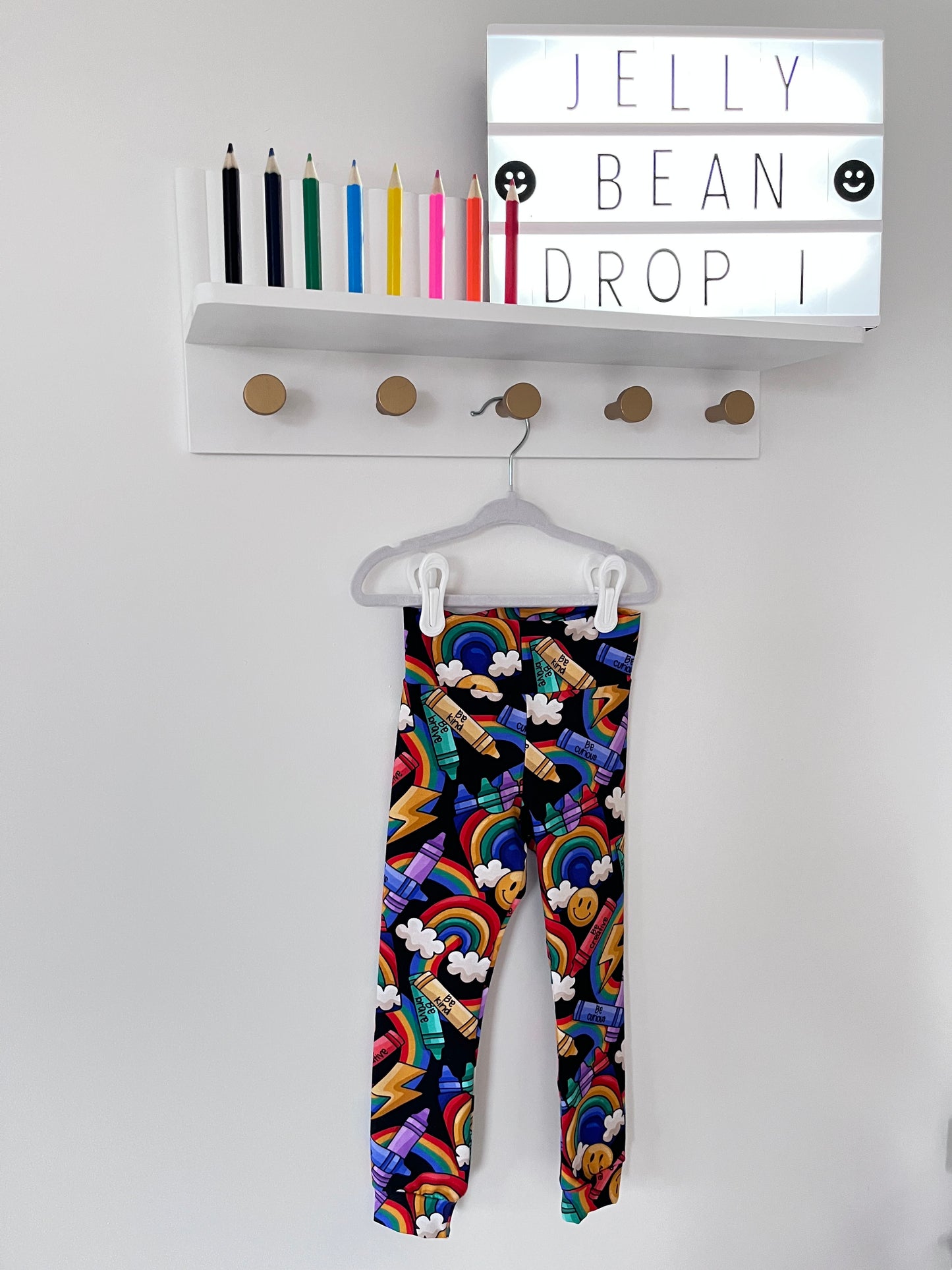 Handmade children’s leggings in a rainbow crayon print, featuring colourful crayons, rainbows, clouds, and positive messages on a dark background.