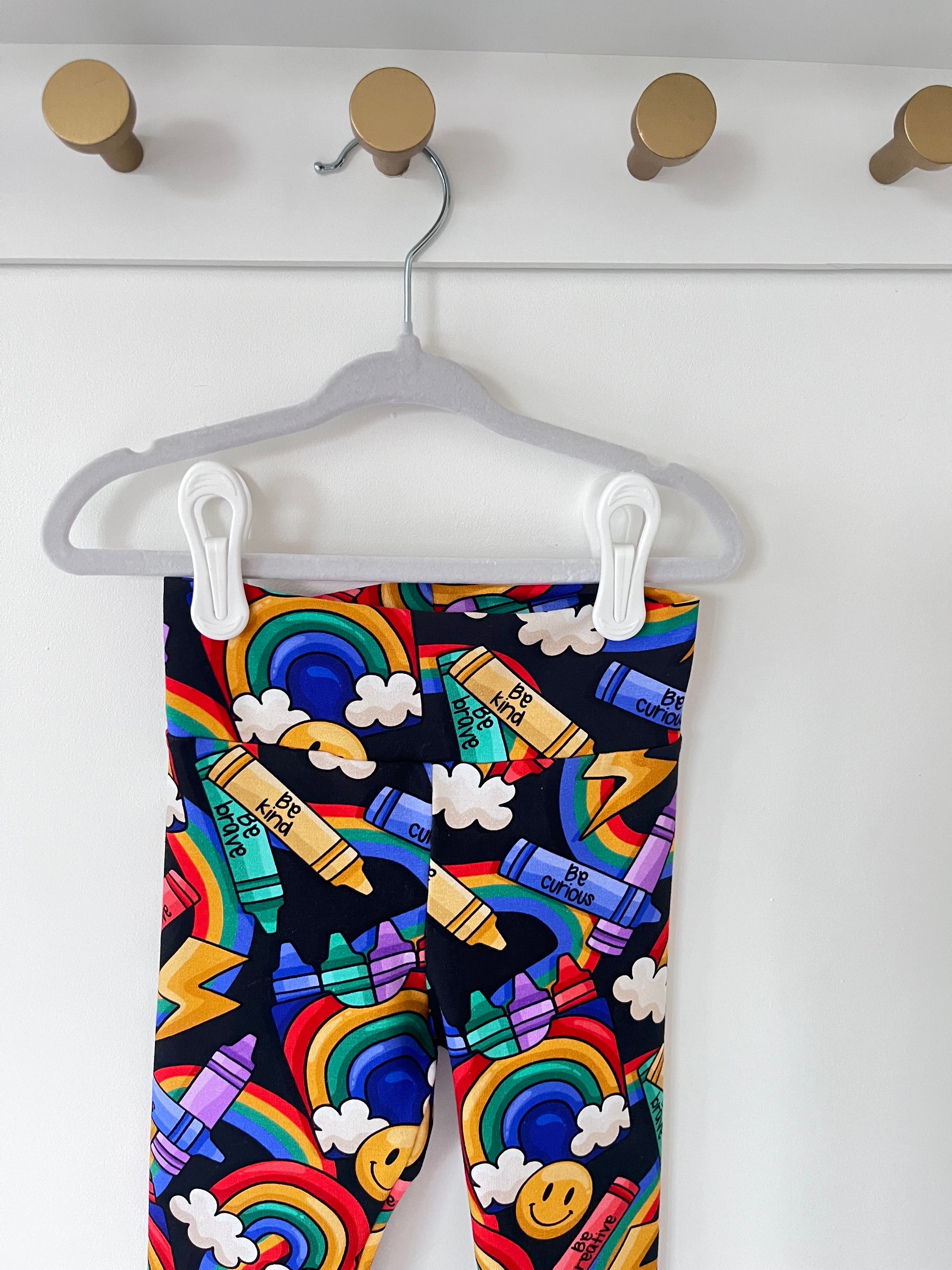 Handmade children’s leggings in a rainbow crayon print, featuring colourful crayons, rainbows, clouds, and positive messages on a dark background.